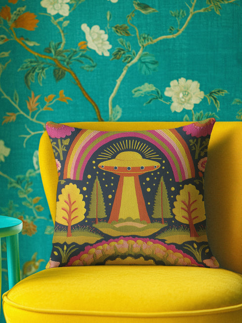 a vibrant yellow chair with a colorful pillow featuring an alien spacecraft and a rainbow, set against a teal floral wallpaper.