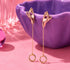 a pair of gold earrings with a hand design, hanging from a purple bowl.