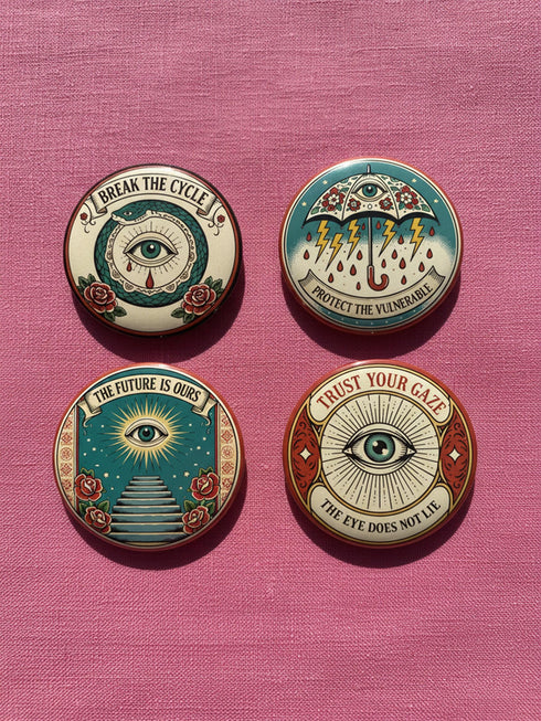 Four 2.25-inch circular metal pinback buttons on a pink textured background. The designs feature vintage tattoo-style art in rust, ochre, gold, and teal with heavy black linework. Designs include a snake Ouroboros "BREAK THE CYCLE," an umbrella eye "PROTECT THE VULNERABLE," a staircase "THE FUTURE IS OURS," and a radial eye "TRUST YOUR GAZE." The pins have a high-gloss finish. Perfect accessory for backpacks, jackets, and lanyards.
