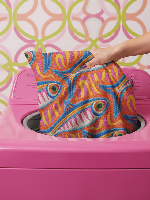 Flat printed square throw pillow cover featuring a faux embroidery texture. The vibrant maximalist design showcases stylized blue, pink, yellow, and white fish swimming in a dynamic, swirling pattern across a bright orange background. The artwork mimics heavy crewelwork yarn and stitching, but the material is a smooth 2D flat print. The pillow is shown as a finished square cover, designed to add bright, colorful eclectic fisherman aesthetic decor to any sofa or seating area.