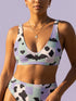 A two piece recycled high waisted swimsuit with a pastel goth checkered print in light lavender purple, pale mint green, and white squares with black cow print spots. The design features small black hearts and silhouetted bats with outspread wings printed throughout. The athletic style crop top has a deep scoop neck and matching thick straps, while the double layered bottoms have a supportive high waistband and cheeky cut with a solid black inner lining.