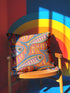 Flat printed square throw pillow cover featuring a faux embroidery texture. The vibrant maximalist design showcases stylized blue, pink, yellow, and white fish swimming in a dynamic, swirling pattern across a bright orange background. The artwork mimics heavy crewelwork yarn and stitching, but the material is a smooth 2D flat print. The pillow is shown as a finished square cover, designed to add bright, colorful eclectic fisherman aesthetic decor to any sofa or seating area.