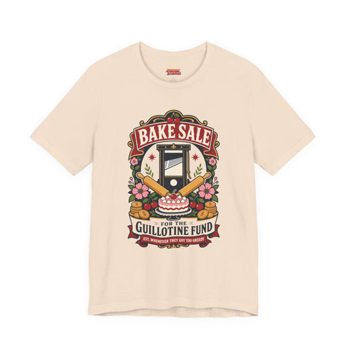 A short sleeve unisex crewneck t-shirt featuring a vintage style emblem graphic centered on the chest. The design features a red banner reading BAKE SALE above a black guillotine. Two crossed wooden rolling pins sit below the guillotine, above a layered pink and white cake with a cherry. The graphic is flanked by pink flowers, cherries, and stacks of gold coins. A bottom banner reads FOR THE GUILLOTINE FUND EST. WHENEVER THEY GOT TOO GREEDY. The shirt comes in light pink, cream, and blue.