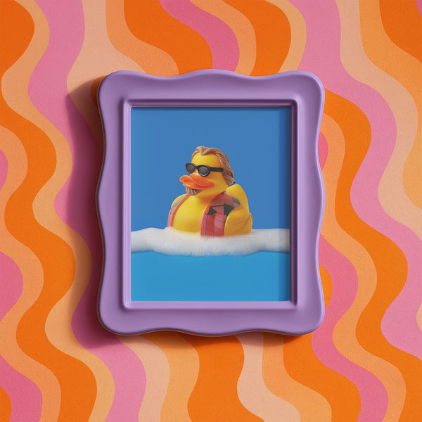 A quirky art print of a rubber duck styled after The Dude from The Big Lebowski, complete with a goatee, sunglasses, and plaid bathrobe. The duck lounges in bubbles, framed in a glossy red frame, with a manicured hand adjusting it against a monochromatic red backdrop.