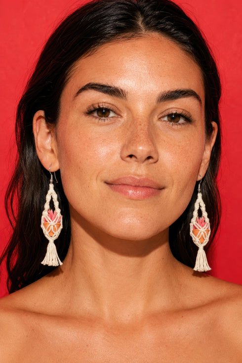 A woman with long dark hair wearing large, dangling earrings against a red background.