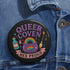 Glossy black pinback button with pastel artwork of a bubbling cauldron, rainbow, potion bottles, and tools. Text reads “Queer Coven, Hex Proud.”