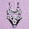 A two piece recycled high waisted swimsuit with a pastel goth checkered print in light lavender purple, pale mint green, and white squares with black cow print spots. The design features small black hearts and silhouetted bats with outspread wings printed throughout. The athletic style crop top has a deep scoop neck and matching thick straps, while the double layered bottoms have a supportive high waistband and cheeky cut with a solid black inner lining.