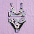 A two piece recycled high waisted swimsuit with a pastel goth checkered print in light lavender purple, pale mint green, and white squares with black cow print spots. The design features small black hearts and silhouetted bats with outspread wings printed throughout. The athletic style crop top has a deep scoop neck and matching thick straps, while the double layered bottoms have a supportive high waistband and cheeky cut with a solid black inner lining.