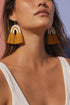 A woman wearing large, yellow and white fringe earrings with a white tassel.