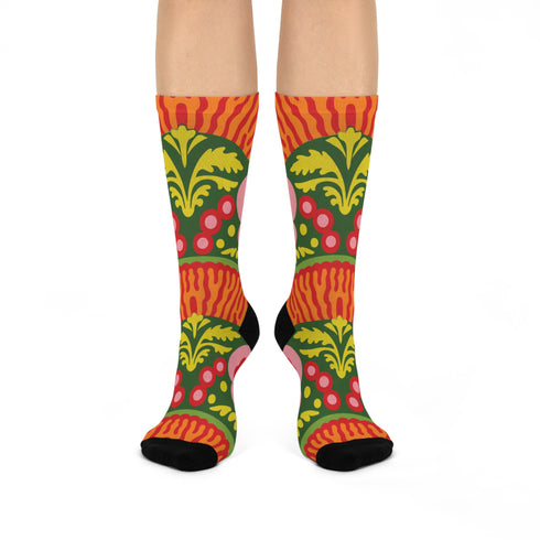 Mid-calf crew sock with a bold retro 70s maximalist botanical print. A deep green base is packed with golden yellow fern-like leaves, pink folk-style flowers with red centers, and clusters of round red and pink berries. Orange and red shell motifs with wavy stripes band the cuff and lower sock. The toe and heel are solid black. The fabric is a soft, stretchy printed knit, made as a one-size unisex statement sock for maximalist and dopamine dressing looks.