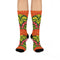 Mid-calf crew sock with a bold retro 70s maximalist botanical print. A deep green base is packed with golden yellow fern-like leaves, pink folk-style flowers with red centers, and clusters of round red and pink berries. Orange and red shell motifs with wavy stripes band the cuff and lower sock. The toe and heel are solid black. The fabric is a soft, stretchy printed knit, made as a one-size unisex statement sock for maximalist and dopamine dressing looks.
