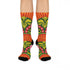 Mid-calf crew sock with a bold retro 70s maximalist botanical print. A deep green base is packed with golden yellow fern-like leaves, pink folk-style flowers with red centers, and clusters of round red and pink berries. Orange and red shell motifs with wavy stripes band the cuff and lower sock. The toe and heel are solid black. The fabric is a soft, stretchy printed knit, made as a one-size unisex statement sock for maximalist and dopamine dressing looks.