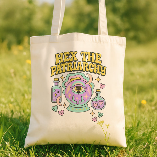 A white tote bag with a colorful graphic design featuring a purple eye, a teapot, and various other whimsical elements.