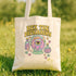 A white tote bag with a colorful graphic design featuring a purple eye, a teapot, and various other whimsical elements.