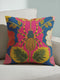 A square maximalist throw pillow with a vibrant, eclectic design. The pillow cover, made of a dark blue linen-feel fabric, features a large, stylized spider at its center. The spider has a striped abdomen in yellow, red, and green, and sits atop a hot pink flower. The design is symmetrical, surrounded by folk art style botanicals, including red, pink, and cream-colored flowers with intricate embroidered-look details. This colorful insect art cushion is a bold accent piece for dopamine decor.