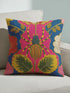 A square maximalist throw pillow with a vibrant, eclectic design. The pillow cover, made of a dark blue linen-feel fabric, features a large, stylized spider at its center. The spider has a striped abdomen in yellow, red, and green, and sits atop a hot pink flower. The design is symmetrical, surrounded by folk art style botanicals, including red, pink, and cream-colored flowers with intricate embroidered-look details. This colorful insect art cushion is a bold accent piece for dopamine decor.