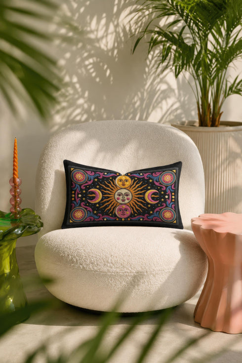 Rectangular 20x12 inch lumbar pillow cover in black featuring printed faux crewel embroidery of a large orange sunburst with a cream face, flanked by pink and yellow crescent moons, a golden moon face above and a pink moon face below, gold stars, blue dots, magenta and blue baroque scroll flourishes, and four corner medallions with golden flowers. Whimsigoth celestial design printed on both sides with a hidden zipper, crafted from soft linen look polyester.