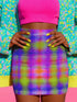 A high-waisted bodycon mini skirt for women featuring a vibrant, pixelated plaid pattern in neon purple, blue, green, and pink, resembling a digital glitch. The skirt is made from a smooth, stretchy performance knit fabric that hugs the body's curves. It has a mid-thigh length and a clean, seamless waistband. This piece of festival and rave wear is available in two finishes: a UV-reactive version that glows under black light, and a glitter knit version with a metallic, holographic sheen.