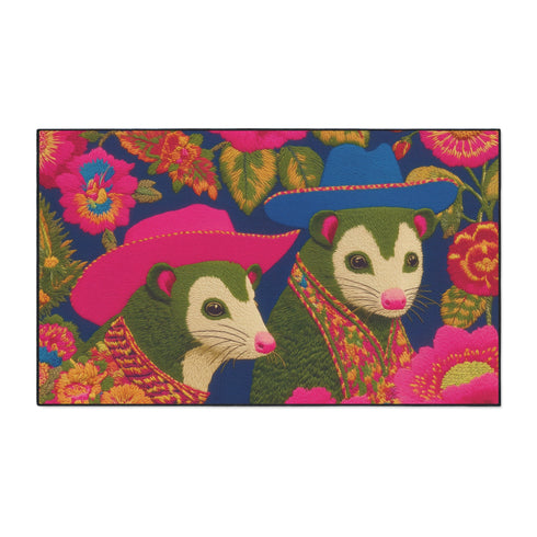 A rectangular non-slip doormat with a black trimmed edge. The mat features a vibrant, colorful folk art illustration on a dark navy blue background with a faux embroidered texture. The design depicts two friendly opossums, rendered in an olive green color with white faces and pink noses. They are surrounded by large, stylized flowers and leaves in shades of hot pink, red, turquoise, and yellow, creating a busy, maximalist pattern. The overall aesthetic is eclectic, whimsical, & highly detailed.