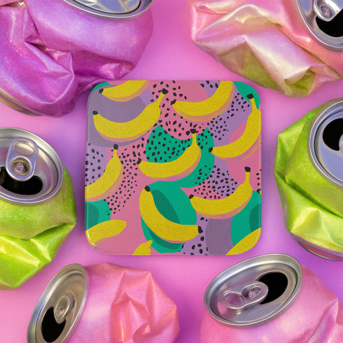 Square drink coaster featuring a playful banana print with bold yellow bananas over a pastel pink, purple, and green abstract background. Made of durable hardboard MDF with a cork backing and a glossy protective topcoat. Measures 3.74 by 3.74 inches, water-repellent and heat-resistant. Perfect for fruit-themed, retro, Y2K, coquette, or dopamine-core decor styles.