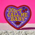 A heart-shaped embroidered patch with a thick red border and a vibrant purple background. In the center, the phrase "DON’T CALL ME BABY" is stitched in a bold, golden-yellow block font. The patch is decorated with small white sparkles, a pair of red cherries with a black musical note, a pair of red lips, and a grey thorny vine design below the text. The overall design has a rebellious, retro, punk aesthetic with a handmade, textured look.