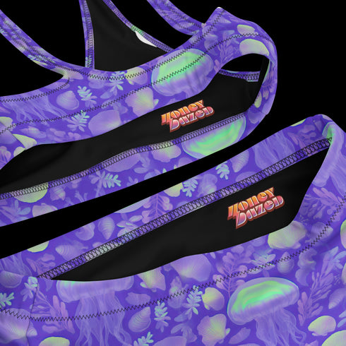 Bralette-style bikini top featuring a high neckline and vibrant jellyfish print in iridescent purples, blues, and greens on a lilac background. Made of recycled polyester and LYCRA XTRALIFE, this double-layered swim top includes removable padding, UPF 50+ protection, and is available in sizes XS to 3XL. Great for raves, beach days, and summer festivals.