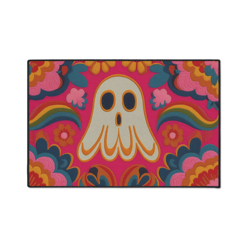 A rectangular polyester doormat with a vibrant, psychedelic design on a hot pink background. In the center is a cute, cartoonish ghost in off-white with yellow and orange outlines; it has large, dark, expressive eyes. The ghost is surrounded by a maximalist pattern of 70s-style floral motifs and puffy clouds in shades of teal, blue, orange, and light pink. Two small, colorful rainbows arc over the ghost's shoulders. The doormat has a durable, textured surface and is framed by a sleek black trim.