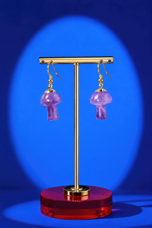 A pair of purple amethyst earrings on a gold stand against a blue background.