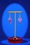 A pair of purple amethyst earrings on a gold stand against a blue background.