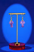 A pair of purple amethyst earrings on a gold stand against a blue background.