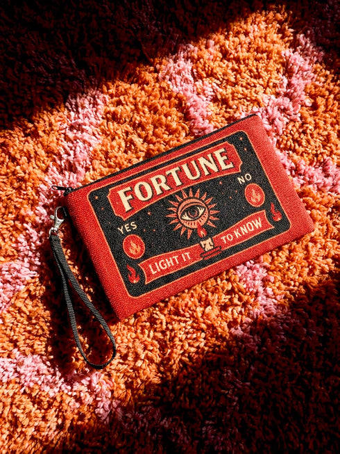 A rectangular red zippered pouch featuring a vintage-style tarot card design. The front displays the word FORTUNE in large beige capital letters. A central illustration shows a mystic eye emitting rays of light above a lit candle flame. The text YES and NO appears on the sides. A banner at the bottom reads LIGHT IT TO KNOW. The bag is crafted from red polyester with a linen-like woven texture, featuring a black zipper and a removable black nylon wrist strap. The interior is white.