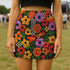 Honey Dazed retro floral mini skirt in a fitted pencil silhouette with high waist. Features a groovy all-over print of oversized flowers, checkers, waves, and bold 70s-inspired shapes in orange, red, purple, green, and yellow. Designed with a soft, sculpting stretch fabric for all-day comfort and drama. A statement piece made for maximalists, festival-goers, and vintage fashion freaks. Perfect for layering with puff sleeves and platform boots.