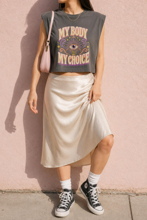 A garment dyed charcoal grey women's muscle tee featuring a slightly cropped boxy fit with structured shoulders and a wide rib collar. The front displays a retro 70s psychedelic graphic printed in purple, orange, and yellow. The text reads MY BODY MY CHOICE surrounding a central eye motif with a radial sunburst, framed by symmetrical mystical swirls and four point stars. The vintage style cotton shirt offers a faded aesthetic, presented on its own without background lifestyle elements.