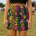 A woman wearing a colorful, patterned mini skirt stands in a grassy field.