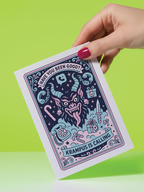 A vertical 5x7 holiday card featuring a retro tattoo style illustration of Krampus in pastel pink, teal, and black ink on shimmery silver pearlescent paper. The central horned demon has a long tongue and is surrounded by vintage rotary phones, daggers, candy canes, and skull gifts. Top text asks Have You Been Good while the bottom banner reads Krampus Is Calling. The interior text reads Let's be honest... Being good is overrated. Merry Christmas.