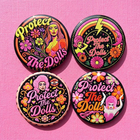 A circular black pinback button featuring the slogan Protect The Dolls in retro script. The design utilizes a high-fidelity trompe-l'œil print style that mimics the texture of raised thread embroidery with satin-stitch detailing. The artwork features vibrant hot pink, rust orange, and golden yellow motifs including drag queens with bouffant hair, 70s style daisies, lightning bolts, and a crescent moon with a face. The surface is smooth and glossy, creating a faux-textured illusion.