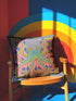A square decorative throw pillow cover featuring a highly symmetrical bright octopus design. The octopus has a turquoise blue body with a diamond patterned head and eight curled tentacles detailed in bright pink and lime green. The background is a repeating diamond argyle pattern in royal blue and light pink. The artwork is a flat two dimensional print that mimics the textured look of intricate crewelwork embroidery. The pillow features a hidden zipper on the bottom edge. No insert included.