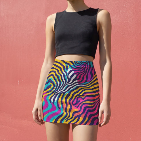 A woman wearing a black crop top and a colorful, zebra-striped mini skirt stands against a pink wall.