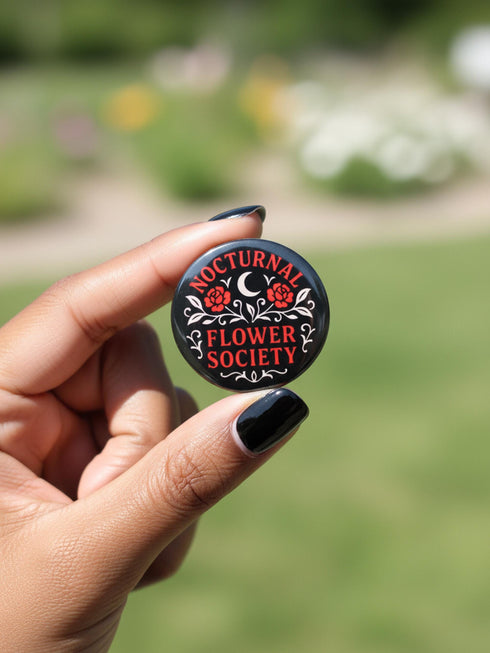 A collection of four glossy black circular pinback buttons featuring striking red and white gothic illustrations. One button shows "Midnight Graveyard Society" text with bats and tombstones. Another reads "Cemetery Picnic Society" with a coffin and umbrella icon. A third features a detailed white skull and red roses with "Memento Mori" text below. The final pin displays "Nocturnal Flower Society" surrounded by floral vines.