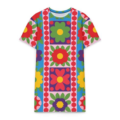 Short-sleeve crew-neck t-shirt dress falling to mid-thigh, with a bold retro patchwork floral all-over print. Large mod daisies in red, purple, yellow, and green sit across a sky blue background, with a central column framing single flowers on purple and pink tiles. Red and pink beaded borders run down the front, and green leaves and more flowers cover the sleeves. The relaxed pull-on dress has a flat printed surface in vivid, high-contrast color.