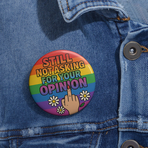 Round glossy pinback button measuring 2.25 inches with a bold rainbow pride flag background. Centered text reads “Still Not Asking For Your Opinion” in black, yellow, blue, and purple letters. Below the text is an illustrated hand with painted red nails giving the middle finger, surrounded by white daisies. The design is printed on tinplate with a scratch- and UV-resistant mylar coating. Button features a strong safety pin backing, perfect for bags, jackets, or pride outfits.