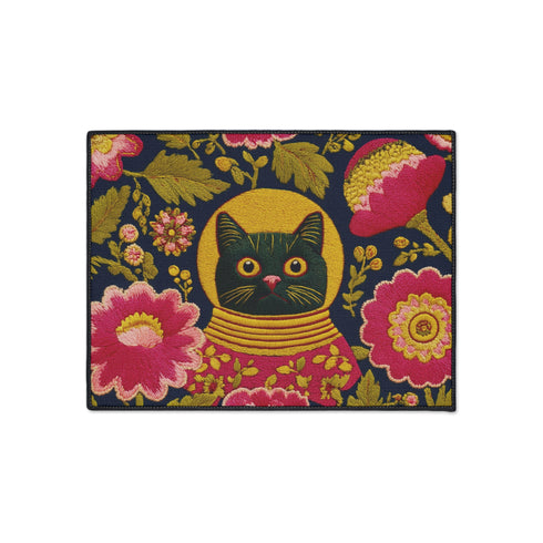 High-fidelity printed doormat featuring a "Space Kitty" design in a tapestry-style faux-texture. A black cat with large yellow eyes wears a golden ribbed space helmet, centered on a deep navy background. The cat is surrounded by oversized, vibrant magenta and pink folk-art flowers with chartreuse and olive green leaves. The design uses a printed illusion to mimic 3D embroidery stitching. The mat is rectangular with a sleek black border and a non-slip backing.