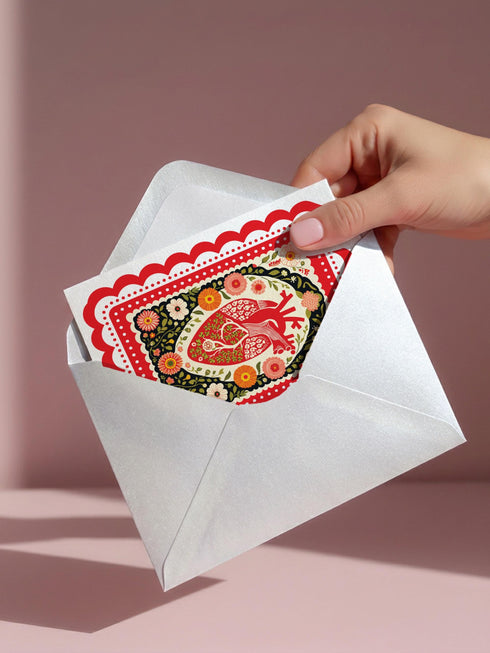 Realistic anatomical heart illustration printed in high contrast ink on a premium 5x7 inch shimmery pearlescent greeting card. The biological heart drawing features detailed arteries, veins, and ventricles, styled with a vintage medical or folk art aesthetic. The cardstock has a visible iridescent sheen. Blank inside valentine card shown with a white peel and seal envelope. Perfect for gothic decor, medical student gifts, cardiology nurse appreciation, and dark academia stationery collections.