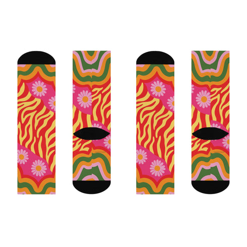 A pair of vibrant crew socks featuring a maximalist 1970s inspired collage pattern. The design includes blocks of hot pink with white daisy flowers and yellow centers, clashing playfully with panels of mustard yellow and orange tiger stripes. Wavy psychedelic lines in grass green and orange frame the top cuff. The socks have a solid black heel and toe cap. The fabric is a smooth, stretchy polyester blend with a flat knit texture and bright colors.