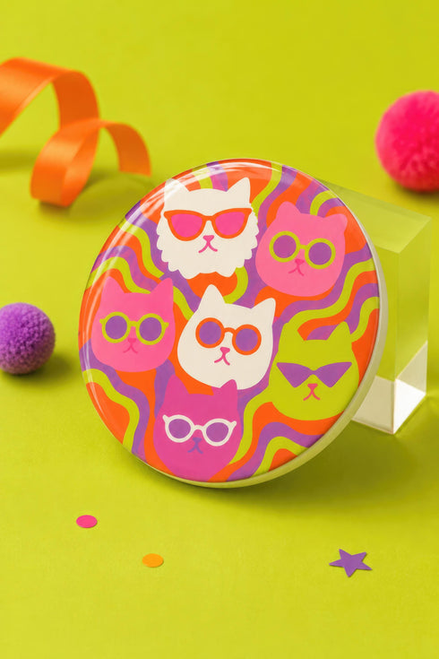 A close-up photograph of a glossy round ceramic coaster featuring a retro 70s psychedelic design. The artwork displays a cluster of six stylized cat face illustrations, each wearing a different pair of sunglasses including retro round and cat-eye shapes. The cats are colored in solid shades of white, hot pink, purple, and lime green. They are set against a vibrant background of wavy, swirling lines in bright orange, red, and purple. The top surface has a highly reflective clear glaze.