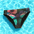 High-waisted bikini bottom with a gothic butterfly print in rich teal, plum, and midnight tones on a black background. Features kaleidoscopic wings forming a central butterfly motif across the front, with a flattering cheeky cut and double-layered fabric. Styled on a turquoise pool backdrop, this moody festival swimwear is perfect for soft goths, rave queens, and dark summer rebels.