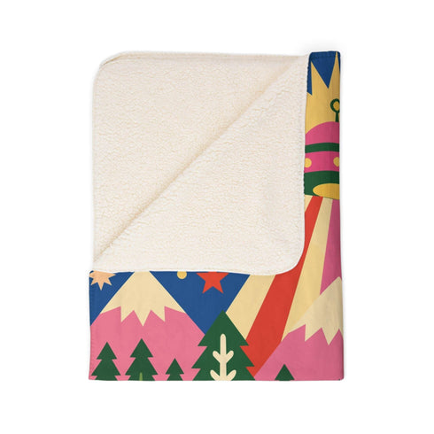 A rectangular velveteen minky blanket with a bright, maximalist design. The top half features a vibrant blue sky with a pink, green, and yellow UFO beaming rays down over hot pink snow-capped mountains. The bottom half shows a grassy green field with a white cow covered in dark spots, surrounded by large, colorful red, pink, and blue retro flowers, pine trees, and a rainbow arch at the very bottom. The reverse side is a fluffy off-white sherpa.