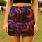 A woman wearing a short skirt with a colorful, abstract pattern of swirls and lines in shades of purple, red, and orange.