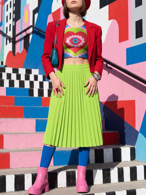 A sleeveless scoop neck crop top featuring a bold all-over printed design. The central graphic is a large bright red heart enclosing a scalloped pink flower shape and a blue evil eye motif in the middle. The background surrounds the heart with mirrored concentric wavy arches and scalloped borders in vibrant shades of lime green, pink, blue, and red. The fitted garment has a smooth athletic texture. Available in a standard matte performance knit or a sparkly silver glitter foil finish.