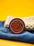 3-inch circular embroidered iron-on patch, cotton–polyester blend; black center with white accent ring, orange inner ring, red outer ring; bold orange stacked lettering says “SMUT SCHOLAR”; merrowed edge. Romance reader patch for spice lovers, indie bookstore fans, and BookTok romantasy crews; makes a great gift for bookish besties with a steamy TBR.